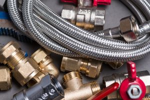 Adjustable spanner with assorted plumbing fittings and hose on grey surface