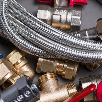 Adjustable spanner with assorted plumbing fittings and hose on grey surface