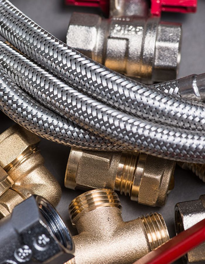 Adjustable spanner with assorted plumbing fittings and hose on grey surface