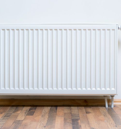 Home radiator heater on the white wall on wooden hardwood floor. Adjustable warming equipment for apartment and home